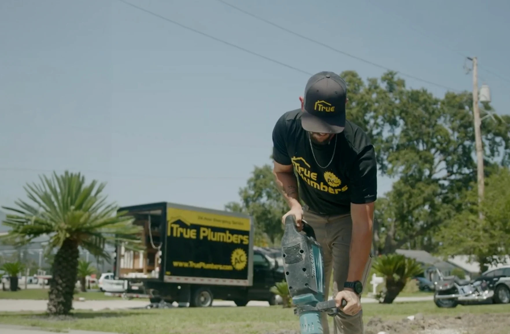 A True Plumbers technician working a jackhammer beside a branded truck